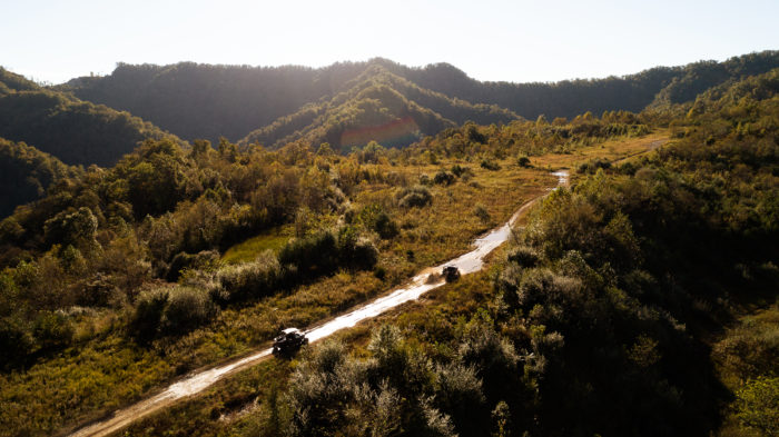 Two ATVs driving down long dirt stretch surrounded by grassy hills and trees