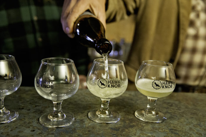 Man pouring a bottle of cider into three glasses with Hawk Knob labels